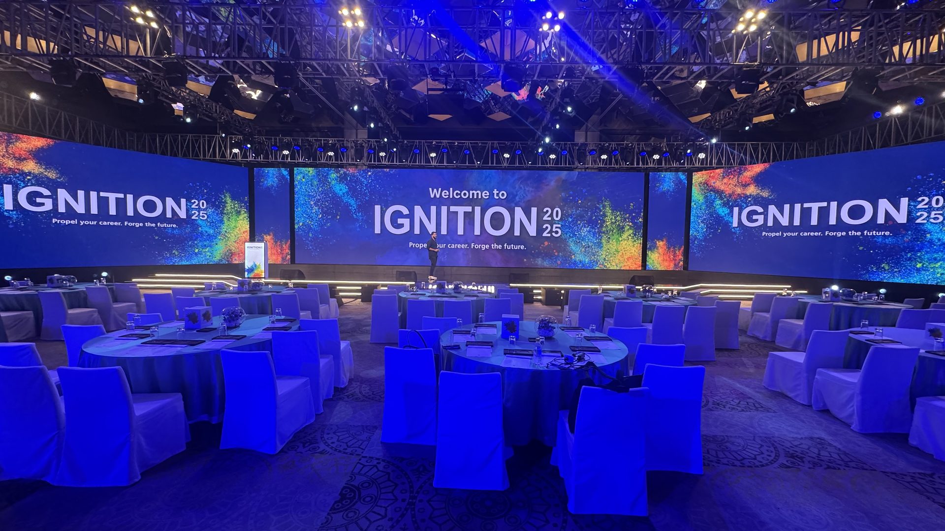 Cabaret-round seating washed in blue ahead of doors, facing the curved Ignition 2025 LED wall